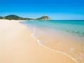 Piękne plaże Cagliari z turkusową wodą i piaszczystym brzegiem, na wzgórzu majaczy biała wieża.