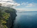 Widok na klifowe wybrzeże z domkami na zboczu i farmą rybną na oceanie. Zastanawiam się, ile się leci na Maderę, by podziwiać takie krajobrazy.