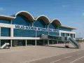 Nowoczesny budynek lotniska Milas-Bodrum International Airport z charakterystycznymi łukami dachu i szklaną fasadą. Obok widoczna rękaw lotniczy i schody.