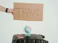 Ręka trzyma tabliczkę z napisem TRAVEL. Obok walizka, globus i paszport. Czy to zapowiedź kolejnych pozytywnych emka travel opinie?
