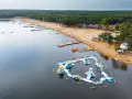Sielpia jezioro tętni życiem. Na piaszczystej plaży wypoczywają ludzie, a w wodzie szaleją na dmuchanych zjeżdżalniach i torach przeszkód.