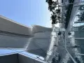 Nowoczesna architektura AUH Zayed International z falującym dachem i szklanymi fasadami odbijającymi niebo i zieleń.