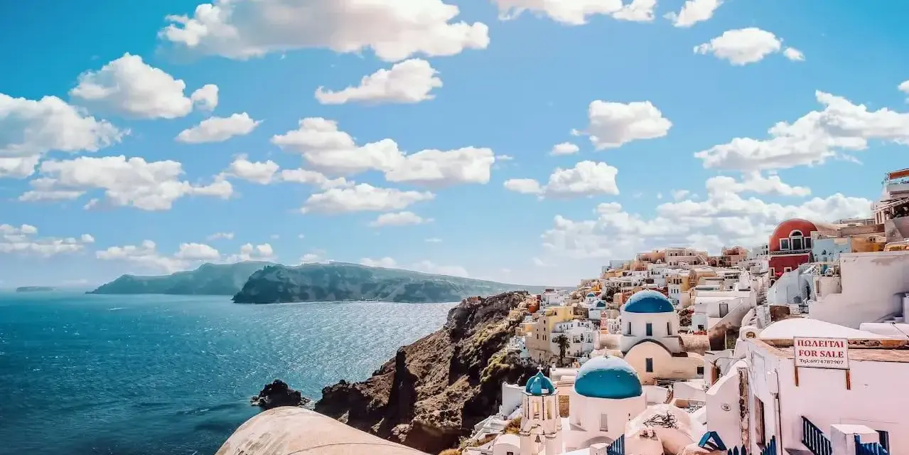 Widok na białe domy z niebieskimi kopułami na Santorini. Zastanawiasz się, ile się leci do Grecji, by podziwiać takie krajobrazy?