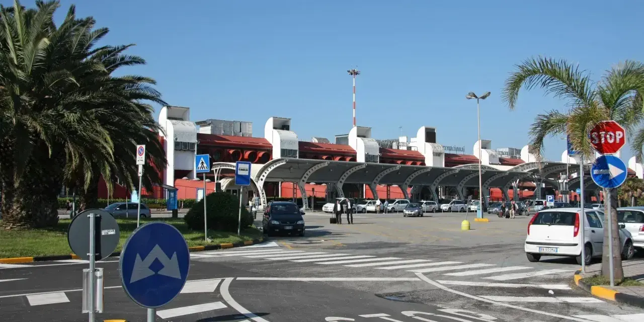 Słoneczny dzień na lotnisku w Kalabrii. Palmy, samochody i nowoczesny budynek terminala.
