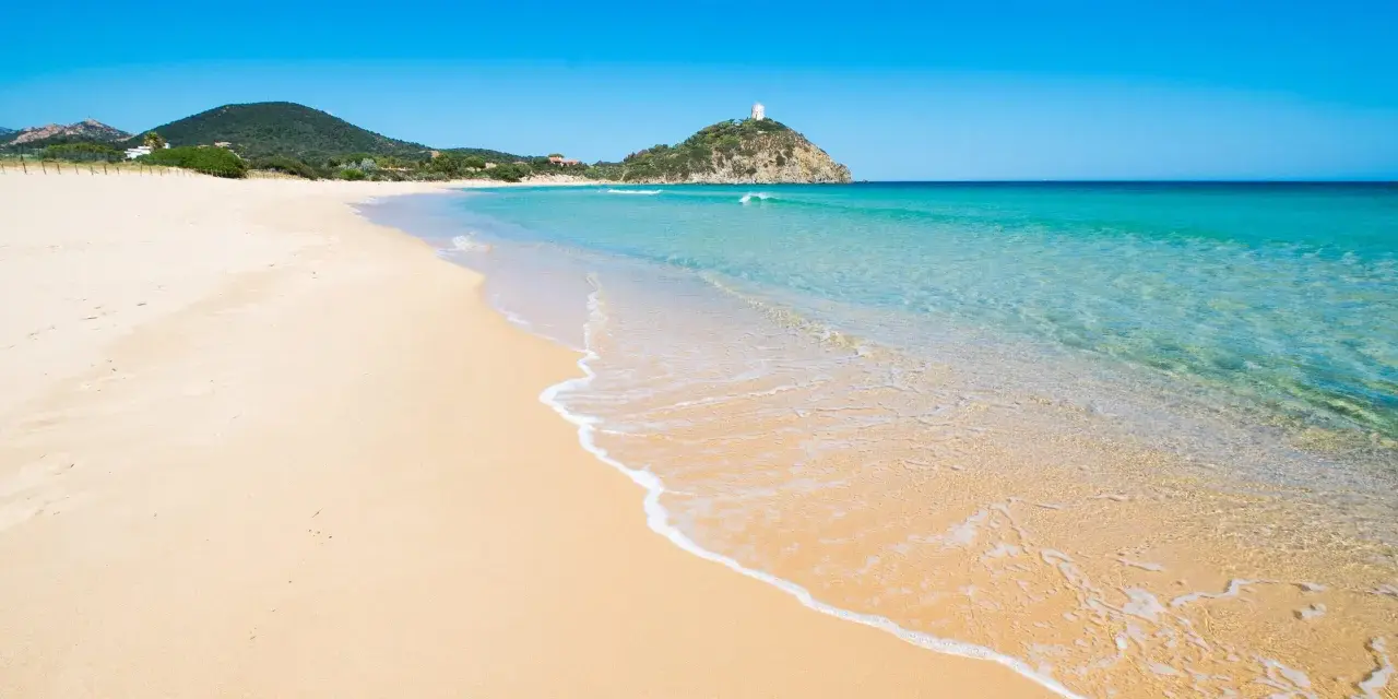 Piękne plaże Cagliari z turkusową wodą i piaszczystym brzegiem, na wzgórzu majaczy biała wieża.
