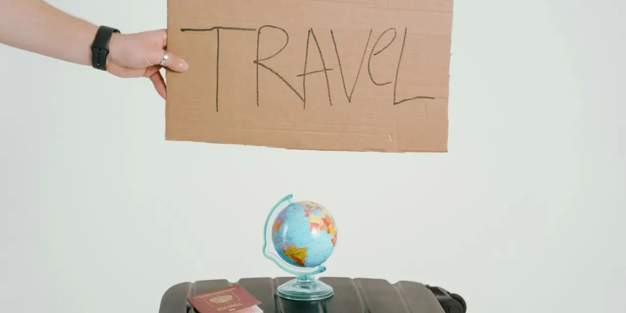 Ręka trzyma tabliczkę z napisem TRAVEL. Obok walizka, globus i paszport. Czy to zapowiedź kolejnych pozytywnych emka travel opinie?