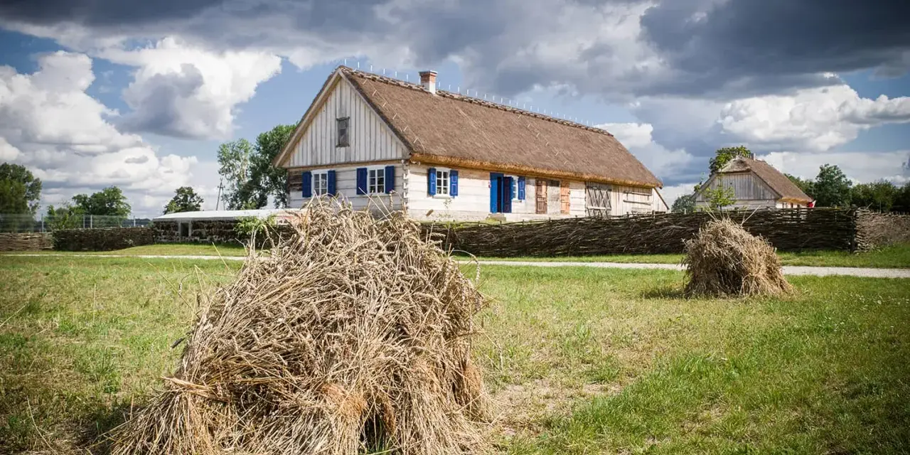 Tradycyjne chaty z krytymi strzechą dachami, jak te w skansenach w Polsce, otoczone plecionymi płotami i stogami siana.
