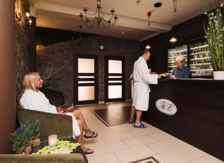 Recepcja w hotelu dla dorosłych. Kobieta w szlafroku siedzi, mężczyzna rozmawia z pracownikiem.
