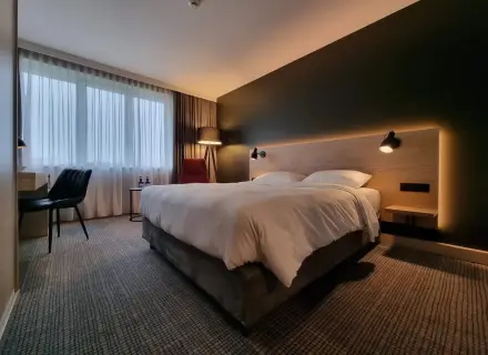 Przytulny pokój w Park Inn Papenburg: wygodne łóżko, designerskie lampy i okna z zasłonami.
