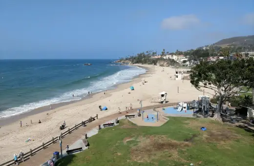 Słoneczny dzień na Laguna Beach. Ludzie spacerują po plaży i drewnianej promenadzie, dzieci bawią się na placu zabaw.