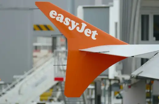 Pomarańczowy statecznik pionowy samolotu easyJet z białym logo, gotowy do przyjęcia bagażu pasażerów.
