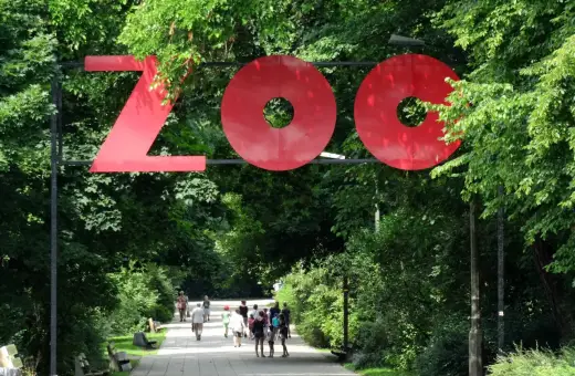 Duże czerwone litery "ZOO" nad alejką w parku. Wiele zoo w Polsce zaprasza na spacer.