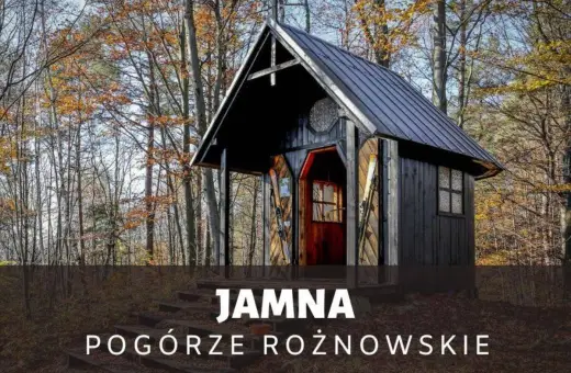 Drewniana kapliczka w lesie, jesienią. Na schodach przed wejściem stoją narty. To urokliwa **Jamna** na Pogórzu Rożnowskim.