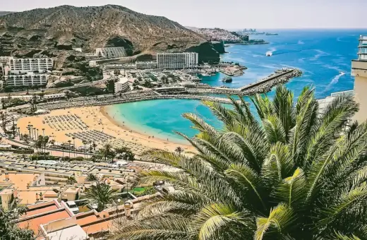 Widok na zatokę z plażą, hotelem i palmami. Zastanawiasz się, ile się leci na Wyspy Kanaryjskie? To idealne miejsce na wakacje!