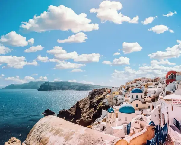 Widok na białe domy z niebieskimi kopułami na Santorini. Zastanawiasz się, ile się leci do Grecji, by podziwiać takie krajobrazy?