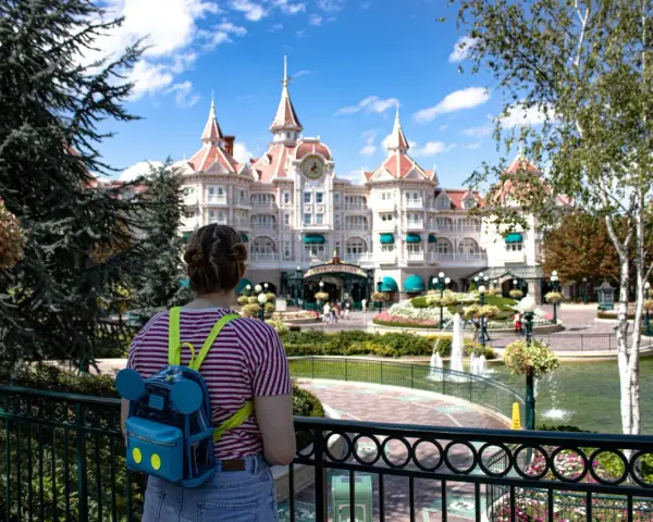 Dziewczyna z plecakiem w kształcie Myszki Miki patrzy na zamek w Disneyland Paris. Bilety do Disneyland Paris czekają na Ciebie!