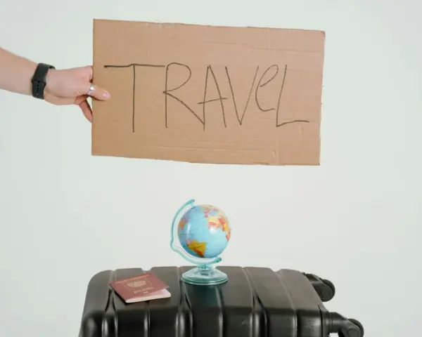 Ręka trzyma tabliczkę z napisem TRAVEL. Obok walizka, globus i paszport. Czy to zapowiedź kolejnych pozytywnych emka travel opinie?