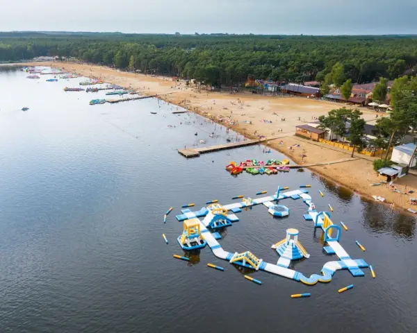 Sielpia jezioro tętni życiem. Na piaszczystej plaży wypoczywają ludzie, a w wodzie szaleją na dmuchanych zjeżdżalniach i torach przeszkód.