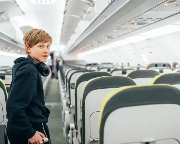Chłopiec z słuchawkami na szyi w pustym samolocie. Zastanawia się, od ilu lat można latać samemu.