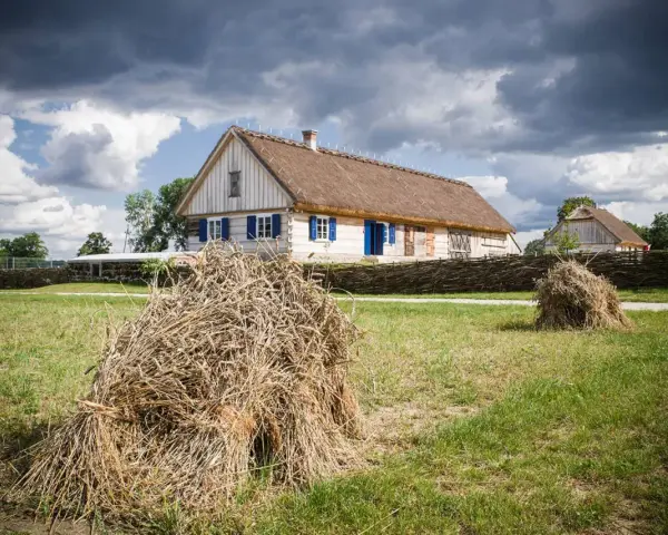Tradycyjne chaty z krytymi strzechą dachami, jak te w skansenach w Polsce, otoczone plecionymi płotami i stogami siana.