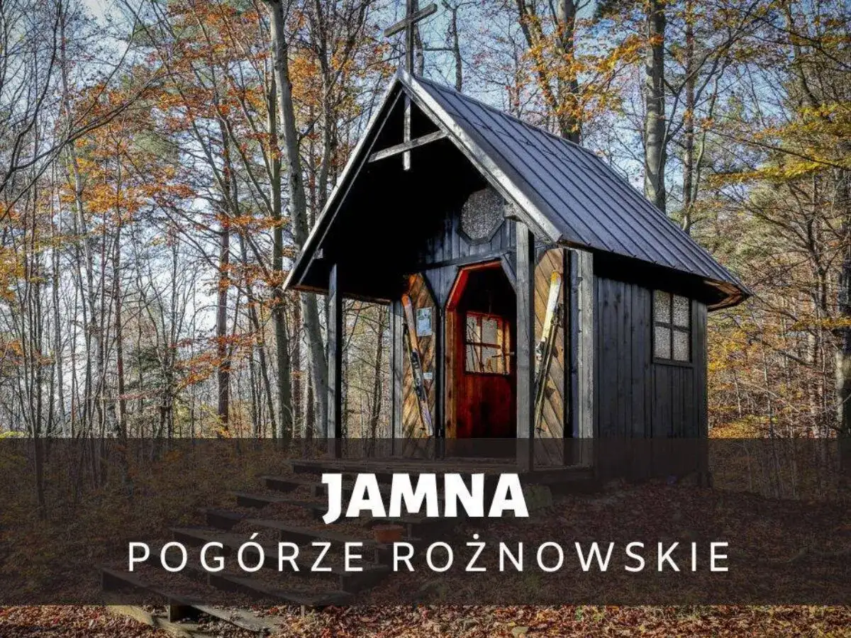 Drewniana kapliczka w lesie, jesienią. Na schodach przed wejściem stoją narty. To urokliwa **Jamna** na Pogórzu Rożnowskim.