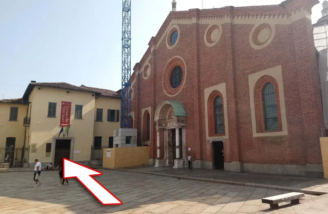 Plac przed kościołem, gdzie można kupić bilety na Ostatnią Wieczerzę. W tle budynek z czerwonym banerem.