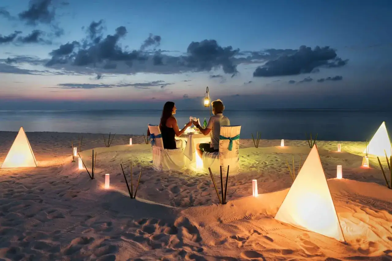 Romantyczna kolacja na plaży, idealne miejsce, gdzie na podróż poślubną. Para wznosi toasty przy świecach i latarenkach.