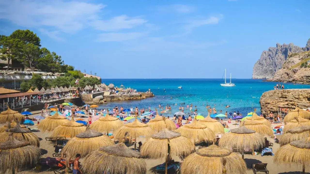 Słoneczna plaża pełna ludzi, parasoli i łodzi. Idealne miejsce na wakacje, potwierdzają to liczne emka travel opinie.