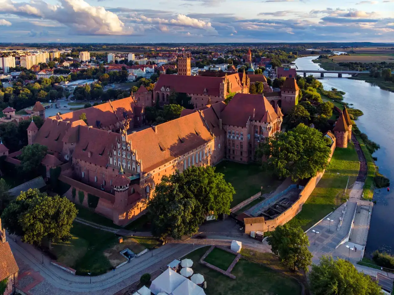 Malbork, największy zamek w Europie, w blasku zachodzącego słońca, z rzeką Nogat w tle.