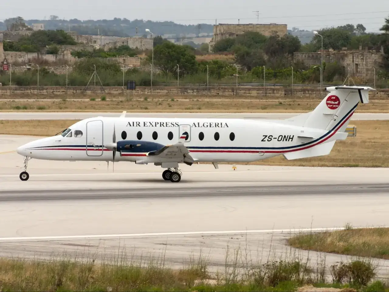 Samolot Air Express Algeria ZS-ONH na pasie startowym, w tle ruiny i zieleń.